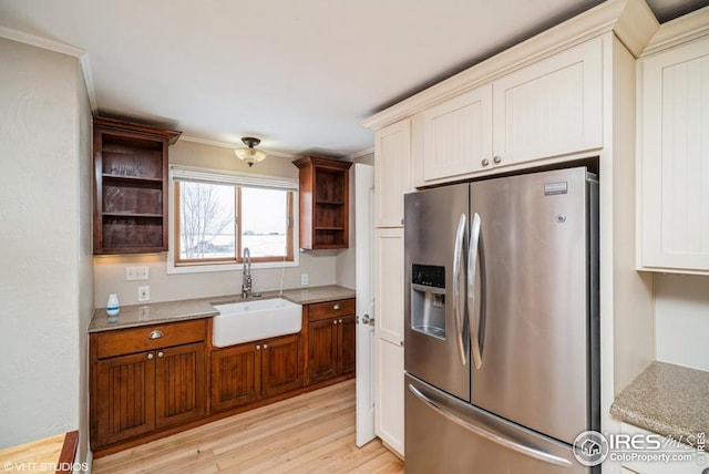 kitchen featuring light wood-style flooring, a sink, light stone countertops, open shelves, and stainless steel fridge