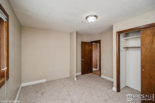 unfurnished bedroom with a textured ceiling, carpet floors, a closet, and baseboards