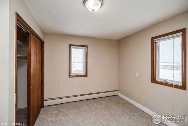 unfurnished bedroom with carpet floors, baseboards, a baseboard heating unit, and a closet