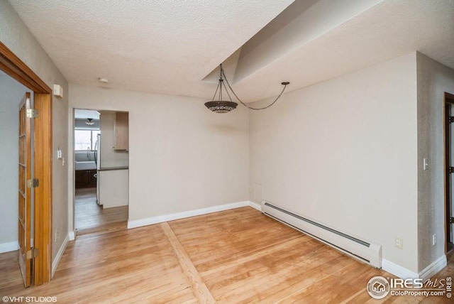 unfurnished dining area featuring light wood-style floors, a baseboard radiator, baseboards, and a textured ceiling