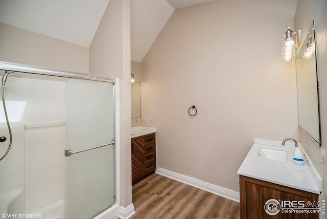 bathroom featuring a stall shower, vaulted ceiling, vanity, wood finished floors, and baseboards