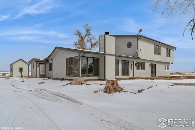 snow covered house featuring a sunroom, a chimney, and an outdoor structure