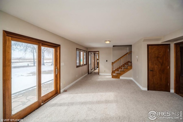 carpeted empty room featuring stairs and baseboards