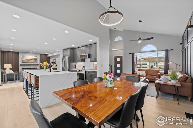 dining area with light wood-style floors, a fireplace, high vaulted ceiling, and recessed lighting