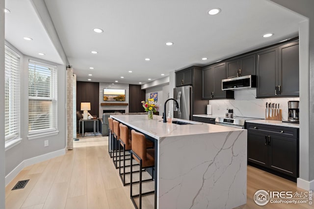 kitchen with tasteful backsplash, visible vents, appliances with stainless steel finishes, light wood-style floors, and a fireplace