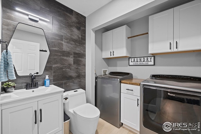 interior space with tile walls, white cabinetry, a sink, light wood-type flooring, and independent washer and dryer