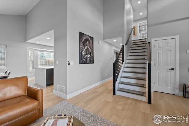 stairway with visible vents, baseboards, wood finished floors, a high ceiling, and recessed lighting