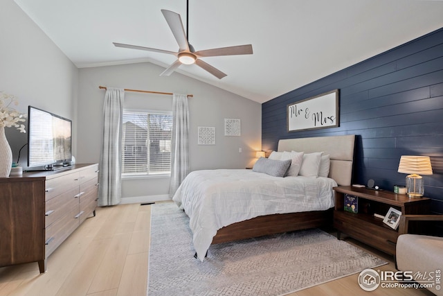 bedroom with light wood finished floors, baseboards, ceiling fan, an accent wall, and vaulted ceiling