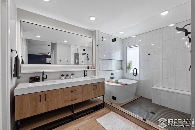 bathroom featuring double vanity, a stall shower, a sink, wood finished floors, and a freestanding tub