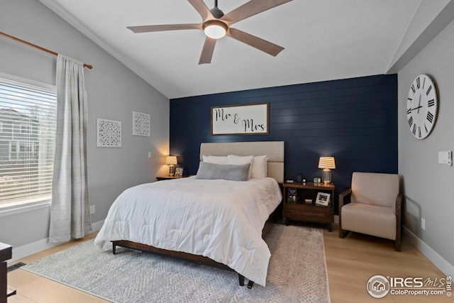 bedroom with baseboards, lofted ceiling, ceiling fan, an accent wall, and light wood-type flooring