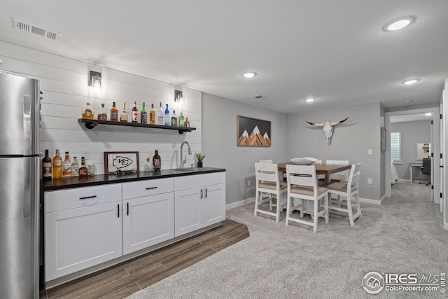 bar featuring recessed lighting, bar, wood finished floors, visible vents, and freestanding refrigerator