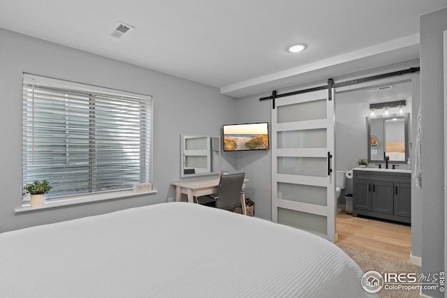 bedroom featuring wood finished floors, visible vents, a sink, and a barn door