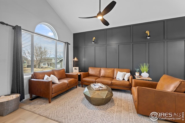 living room featuring ceiling fan, a decorative wall, high vaulted ceiling, and wood finished floors