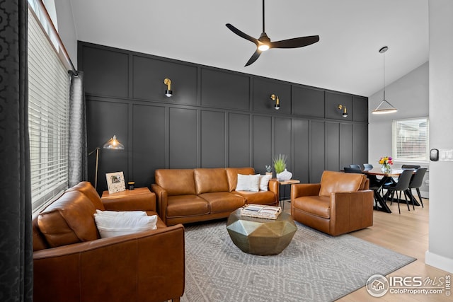 living room featuring ceiling fan, light wood-style flooring, high vaulted ceiling, and a decorative wall