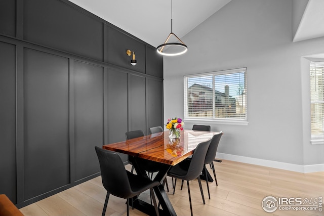 dining room with high vaulted ceiling, light wood-style flooring, and baseboards