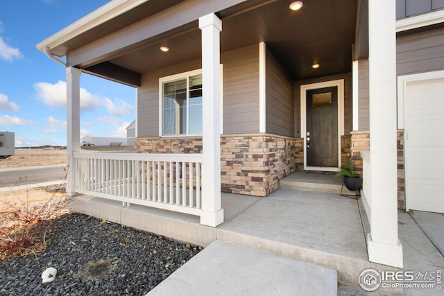 view of exterior entry with a garage, covered porch, and stone siding