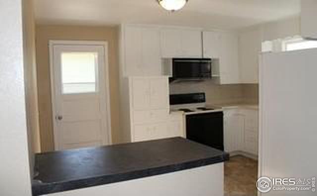 kitchen featuring freestanding refrigerator, white cabinets, black microwave, range with electric stovetop, and dark countertops