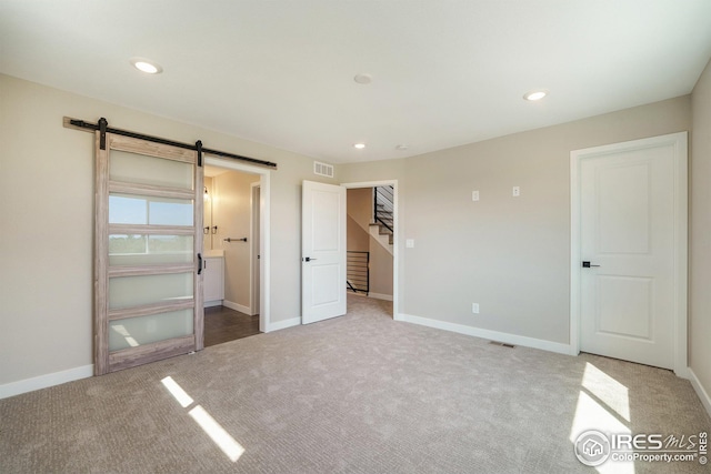 unfurnished bedroom featuring a barn door, carpet flooring, visible vents, and recessed lighting