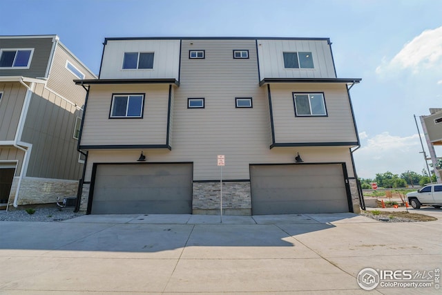townhome / multi-family property featuring concrete driveway, stone siding, and an attached garage