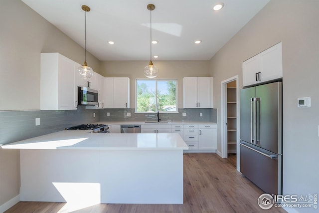 kitchen with stainless steel appliances, light countertops, backsplash, a sink, and a peninsula