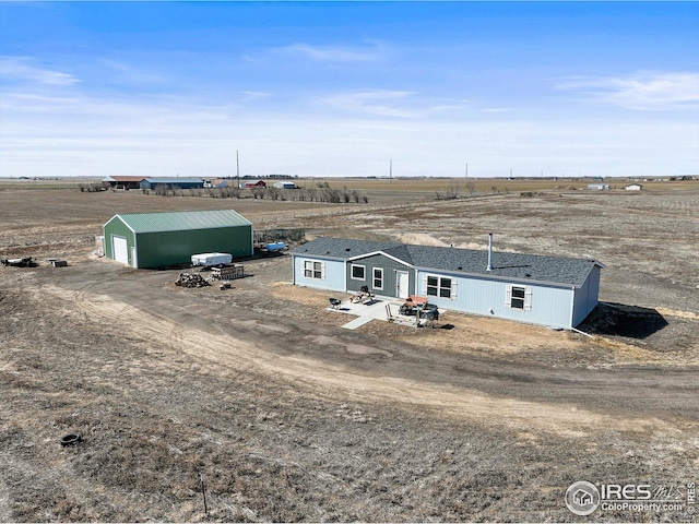 view of front of property with dirt driveway, a detached garage, a rural view, and an outdoor structure