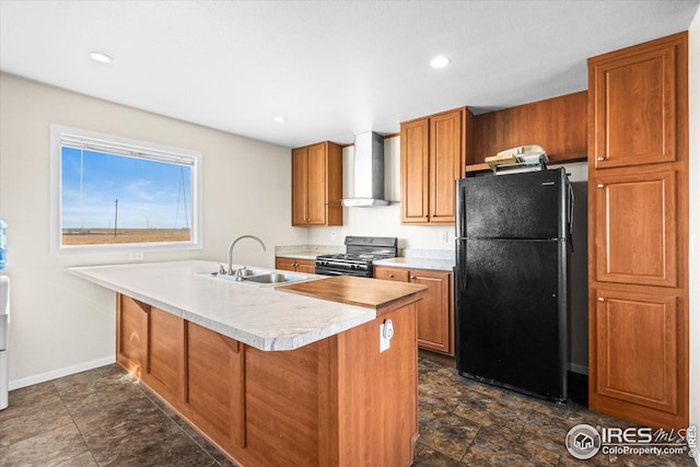 kitchen featuring brown cabinets, freestanding refrigerator, gas stove, a sink, and wall chimney range hood