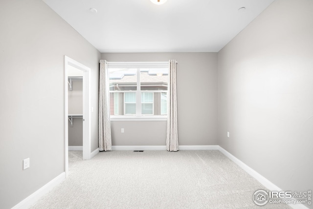 unfurnished bedroom with carpet flooring, a walk in closet, baseboards, and visible vents