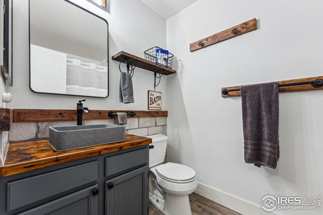 bathroom featuring toilet, vanity, baseboards, and wood finished floors