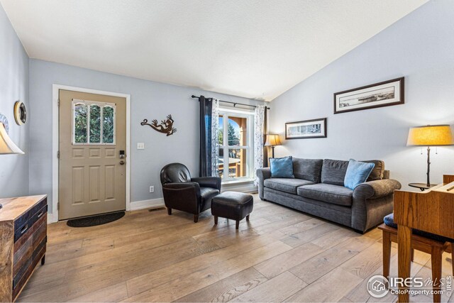 living area with visible vents, baseboards, vaulted ceiling, and light wood finished floors