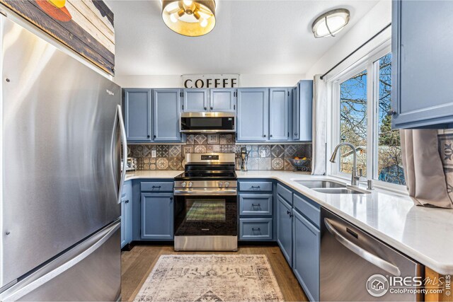 kitchen featuring blue cabinets, a sink, tasteful backsplash, appliances with stainless steel finishes, and light countertops