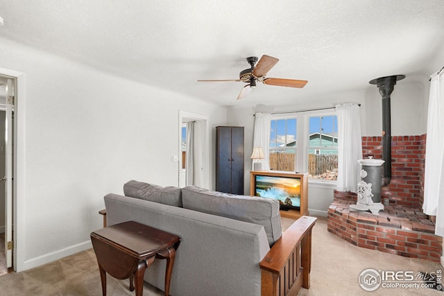 living room featuring a wood stove, light carpet, ceiling fan, a textured ceiling, and baseboards