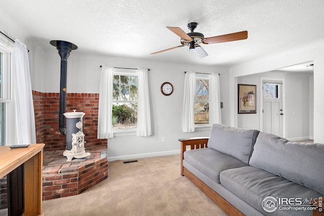 living room featuring visible vents, a ceiling fan, a wood stove, a textured ceiling, and carpet floors