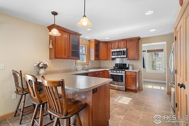 kitchen with stainless steel appliances, a peninsula, a sink, brown cabinets, and glass insert cabinets