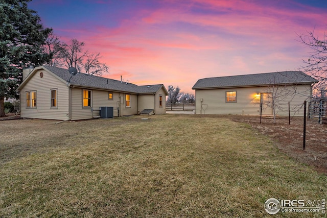 back of property at dusk with central AC, a yard, and fence