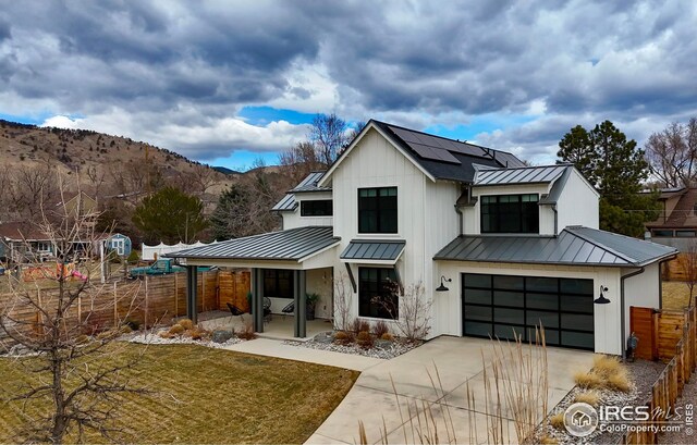 modern farmhouse with concrete driveway, a standing seam roof, roof mounted solar panels, fence, and metal roof