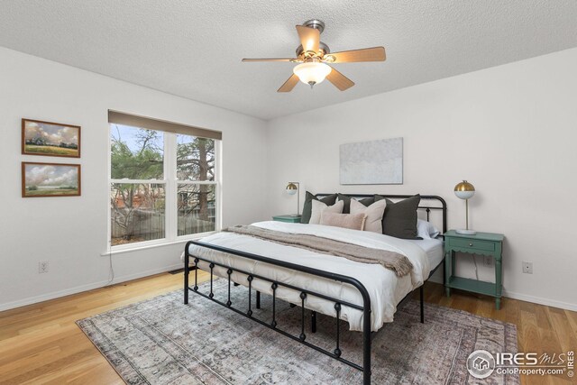 bedroom with a textured ceiling, ceiling fan, wood finished floors, and baseboards