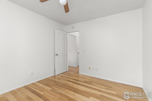 unfurnished room featuring light wood-type flooring, a textured ceiling, baseboards, and a ceiling fan