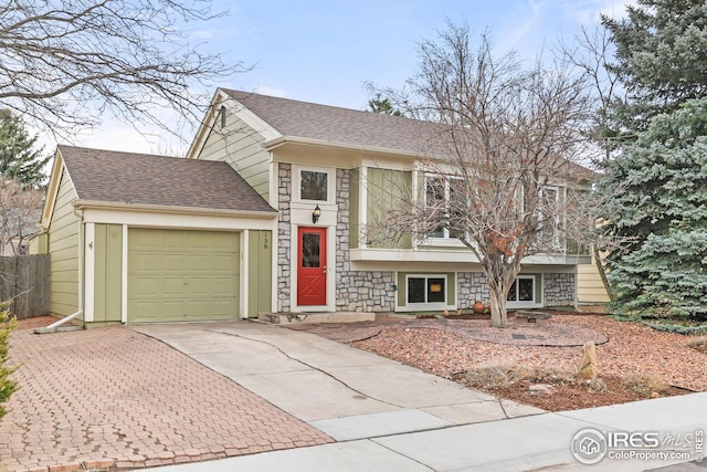 tri-level home with an attached garage, a shingled roof, fence, concrete driveway, and stone siding