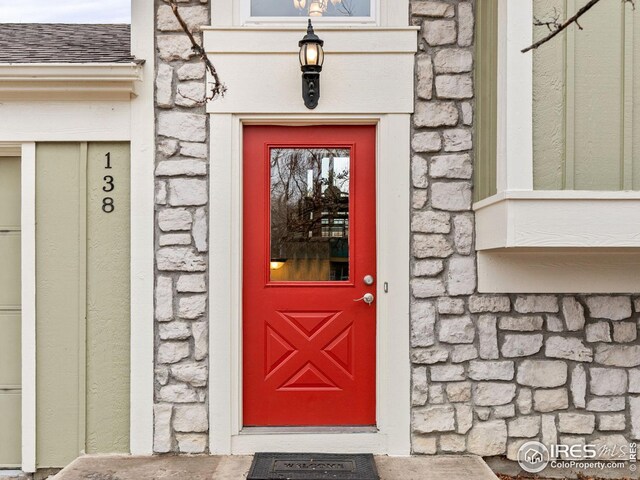 entrance to property with stone siding and roof with shingles