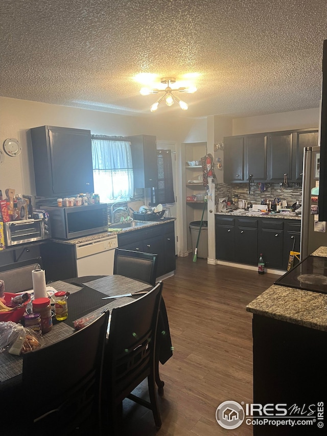 kitchen featuring dark wood-type flooring, freestanding refrigerator, a sink, white dishwasher, and backsplash