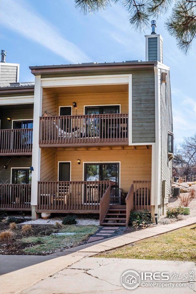 view of front facade featuring central AC unit, a chimney, and a balcony