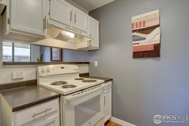 1105 Bacchus Dr Unit 8, Lafayette, CO 80026 - kitchen featuring white range with electric cooktop, dark countertops, white cabinetry, under cabinet range hood, and baseboards