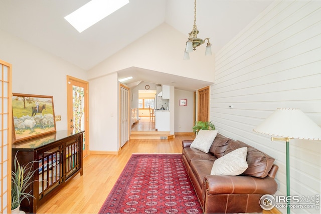 living area featuring a skylight, baseboards, high vaulted ceiling, and wood finished floors