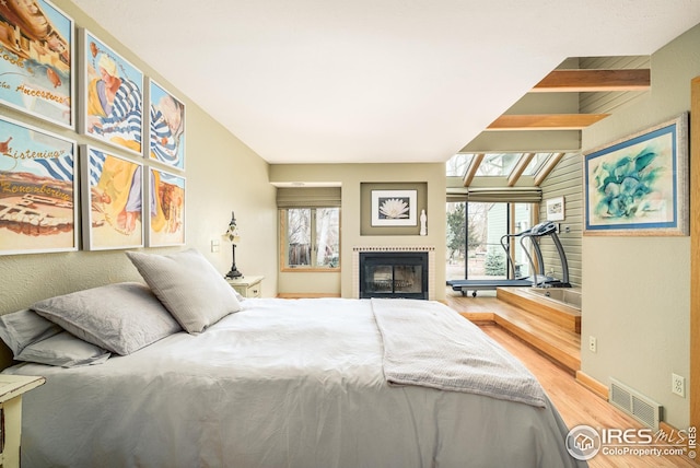 bedroom with baseboards, visible vents, a glass covered fireplace, lofted ceiling with skylight, and wood finished floors
