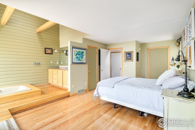 bedroom with ensuite bathroom, visible vents, and light wood-style floors