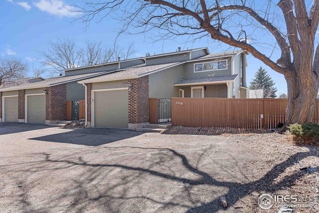 view of front of home with driveway, a fenced front yard, roof with shingles, an attached garage, and brick siding