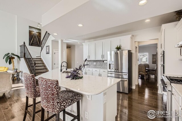 5541 Tullamore Ct, Timnath, CO 80547 - kitchen featuring stainless steel appliances, dark wood-type flooring, a kitchen bar, white cabinets, and light stone counters