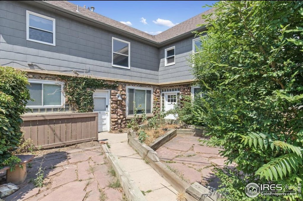 back of house featuring stone siding and a garden