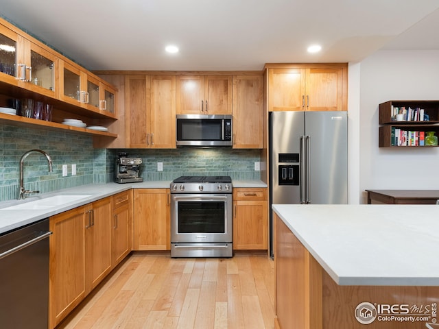 kitchen featuring light wood-style flooring, a sink, decorative backsplash, light countertops, and stainless steel appliances