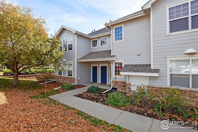 townhome / multi-family property with stone siding and a shingled roof